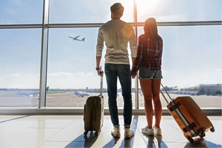 Vuelos - Pareja observando aviones desde una ventana del aeropuerto